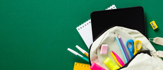 Backpack with colorful school stationery and digital tablet on green table. Back to school concept.