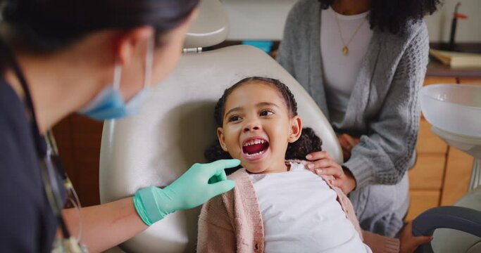 Happy and cheerful little girl at the dentist for annual routine checkup. Dental assistant looking at a young clients oral hygiene at a clinic. Mother supporting her daughter at the orthodontists