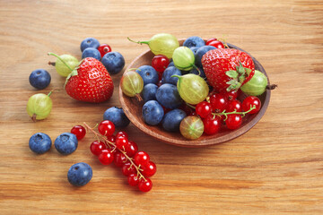 Berries mix in in a heart shaped bowl spilled on rustic wooden table