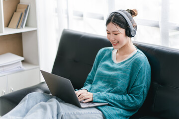 Smart and positive Asian female freelancer or female college student sitting on sofa with laptop. Study from online webinars or home courses. Video calling and chatting