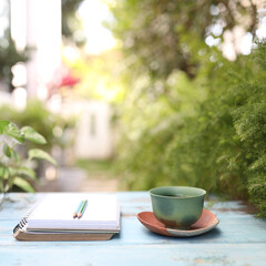 Green tea cup with notebook and pencil on blue wooden table