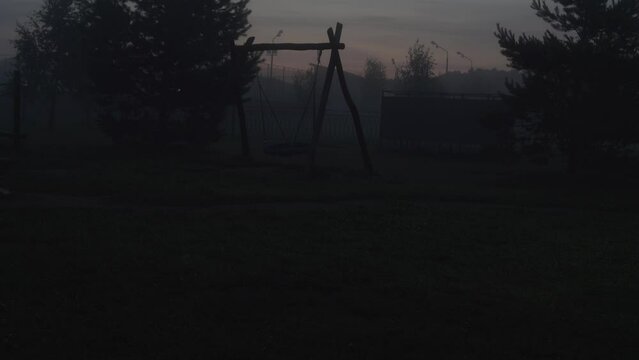 Empty swing on children's playground swinging at foggy night. Horrible poltergeist and ghost concept