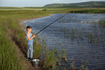 Little boy is fishing at sunset on the lake. Summer holidays in a village. Rest in nature, away from the city
