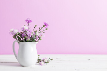 Beautiful bouquet of wild summer flowers in vase against purple wall.