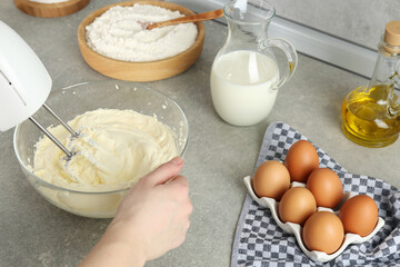 Woman whipping white cream with mixer at light grey table, closeup