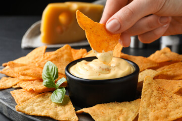 Woman dipping crispy nacho into delicious cheese sauce at table, closeup - obrazy, fototapety, plakaty