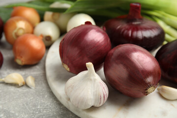Fresh onion bulbs, leek and garlic on grey table, closeup
