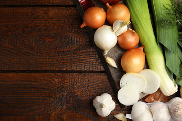 Fresh onion bulbs, leeks, garlic on wooden table, flat lay. Space for text