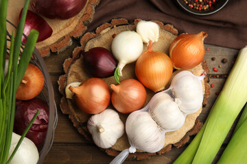 Fresh onion bulbs, leeks and garlic on wooden table, flat lay