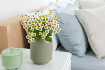 Beautiful bouquet of chamomile flowers on white nightstand in bedroom, space for text. Interior element