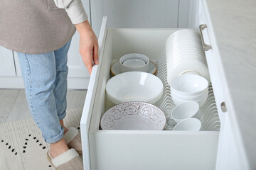 Woman opening drawer with plates and bowls in kitchen, closeup