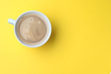 White mug of freshly brewed hot coffee on yellow background, top view. Space for text