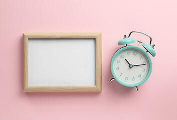 Blank white board with alarm clock on light pink background, flat lay. Space for text