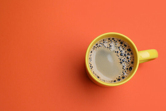 Yellow mug of freshly brewed hot coffee on orange background, top view. Space for text