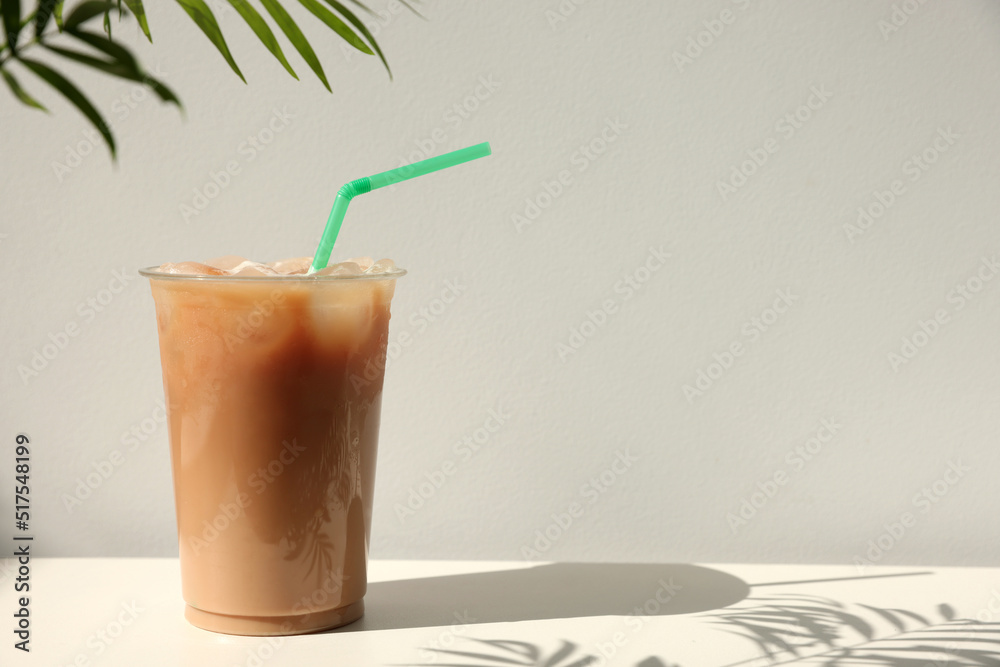 Wall mural Plastic takeaway cup of delicious iced coffee on white table under sunlight, space for text