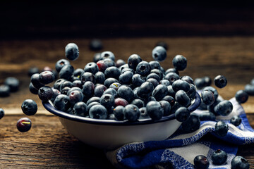Fresh blueberries in an enamel bowl on a wooden rustic table, close up view. Levitating blueberries