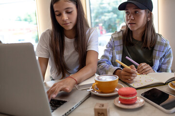 Two girls during the break, drinking coffee and eat, using modern devices, look at the laptop and talk