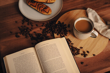 Taza de Café en una mesa de café de madera, con bollos de chocolate, granos de café, un libro abierto, rústico