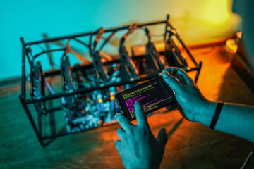 Close up of programmer's hands while adjusting cryptocurrency mining rig to optimal settings with mobile phone