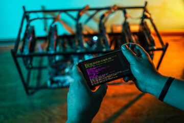 Close up of programmer's hands while adjusting cryptocurrency mining rig to optimal settings with mobile phone