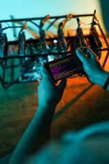 Male programmer adjusting cryptocurrency mining rig to optimal settings with mobile phone