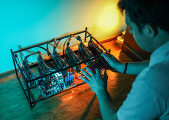 Male programmer adjusting cryptocurrency mining rig to optimal settings with mobile phone