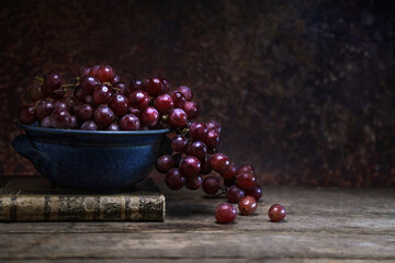 Fresh red grape in a blue bowl with a vintage bood on wooden board table and background - dark and...