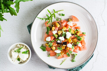 Salad of fried eggplant, tomato and feta cheese on a plate. Homemade lunch. Top view. Close-up