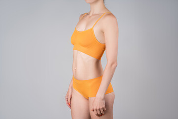 Slim woman in yellow underwear on gray background