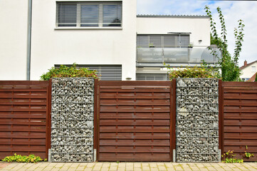 Moderner Sichtschutzzaun abwechselnd aus mit Naturstein gefüllten Gabionen aus verzinktem Stahlgitter und lasierter Holzbretterverschalung um ein bebautes Grundstück © Hermann