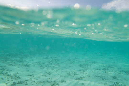 Abstract split level underwater shot of turquoise clear water, white sand coral reef and blue sky 