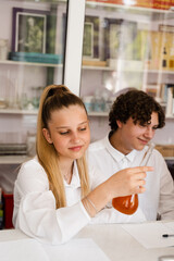 Chemistry lesson. Schoolgirl and classmates holds flask for experiments and smiles in the laboratory. School education.