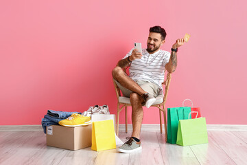 Obraz premium Handsome man with credit card and mobile phone on pink background. Online shopping
