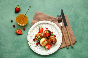 Plate with cottage cheese pancakes, berries and bowl with honey on green background