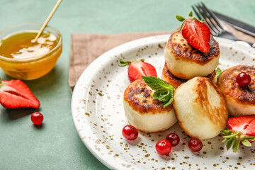 Plate with cottage cheese pancakes, berries and mint leaves on green background, closeup