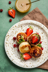 Plate with cottage cheese pancakes, berries and bowl with honey on green background