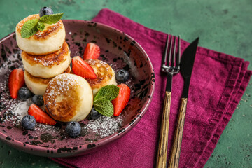 Plate with delicious cottage cheese pancakes, cutlery and napkin on green background