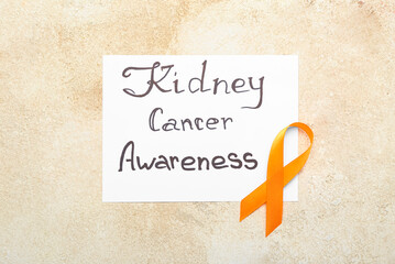 Paper sheet with text KIDNEY CANCER AWARENESS with orange ribbon on grunge background