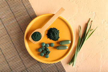Plate with spirulina powder, pills and spoon on beige background