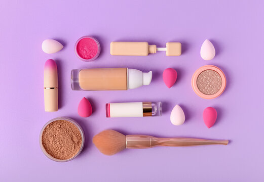 Set of cosmetics, makeup sponges and brush on lilac background