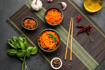 Composition with bowls of tasty korean carrot salad and ingredients on dark background