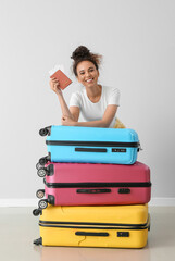 Female African-American tourist with passport and suitcases near light wall