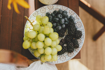 Fresh blueberries, blackberries and grapes in sunlight on ceramic plate in rustic room. healthy...