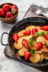 Frying pan with mini pancakes and strawberry on table