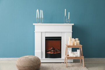 Electric fireplace, pouf and stepladder with candles near blue wall