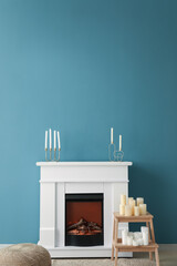 Electric fireplace and stepladder with candles near blue wall