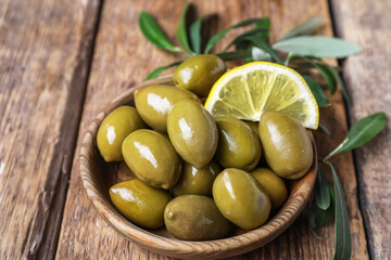 Bowl of tasty green olives with lemon slice on wooden background, closeup