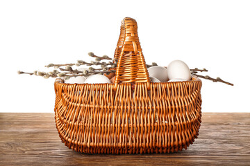 Wicker basket with chicken eggs and pussy willow branches on wooden table against white background