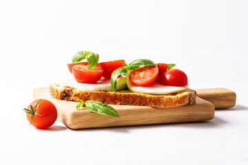 Juicy aromatic caprese sandwich with basil leaves, cherry tomatoes and mozzarella cheese on white background close up. Healthy tasty food concept.