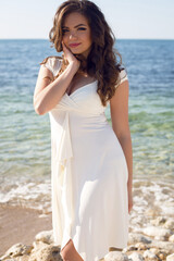 Fototapeta na wymiar Young beautiful brunette woman in white dress walking near the sea